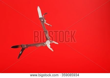 Multitool Is A Multi-functional Tool On A Red Background. The Concept Of An Open, Flying Multi-tool 