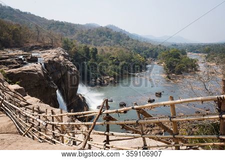 A Huge Waterfall Athirapally In Kerala, India. White Streams Of Water Of The Waterfall Break Into Sm