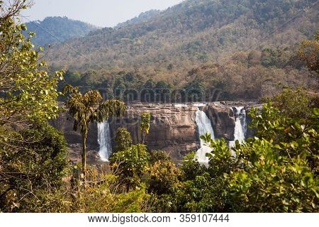A Huge Waterfall Athirapally In Kerala, India. White Streams Of Water Of The Waterfall Break Into Sm