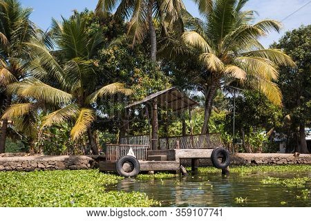 Canal Shore Of A River In The Tropics Of India, Alapuzha, Kerala. Green Shore With Palm Trees And Bu