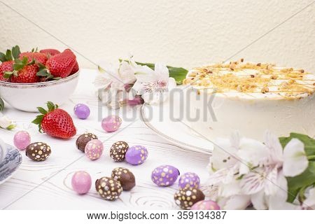 Cake Covered With White Cream And Nuts, Strawberries And Chocolate Eggs In A Multi-colored Falge.