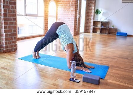 Middle age beautiful sportwoman standing on mat practicing yoga doing dolphin pose at gym