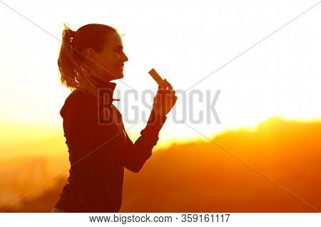 Silhouette Of Runner Woman Eating Energy Bar After Running At Sunset In The Mountain