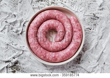 high angle view of a rolled botifarra, a pork meat sausage typical of Catalonia, Spain, in a plate, on a white textured textile background