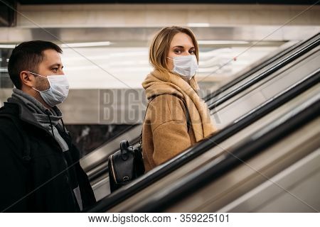 Side View Of Young Man And Woman In Medical Masks On Escalator In Subway. Coronavirus Pandemic.