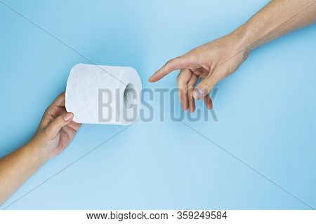 Female Hand Gives Toilet Paper Roll To Male Hand On Blue Background, Top View, Flat Lay. Panic Buyin