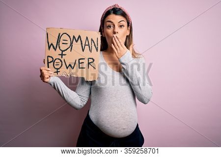 Young brunette woman pregnant expecting baby holding banner asking for women power cover mouth with hand shocked with shame for mistake, expression of fear, scared in silence, secret concept
