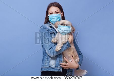 Indoor Shot Of Woman Dresses Denim Jacket Protective Flumask Holds Dog Pet In Medical Mask. Coronavi