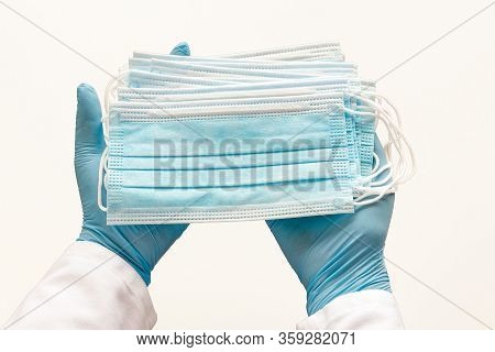 Hands Of Medic Wearing Blue Latex Gloves Holding Surgical Ear-loop Masks On White Background. Protec