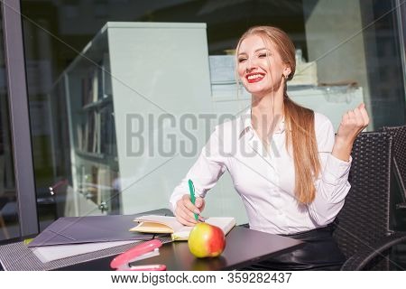 Young Student Shows Hurrah Gesture Sitting At The Table Of The University Cafe.