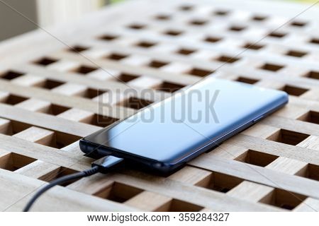 Brecht/belgium - April 1 2020: A Portrait Of A Smartphone With A Usb Cable In Its Port Lying On A Ta