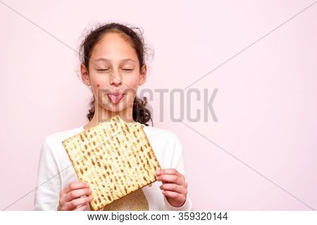Portrait Of The Cute Teenager Girl Holding Matzah And Shows Tongue. Jewish Child Eating Matzo Unleav