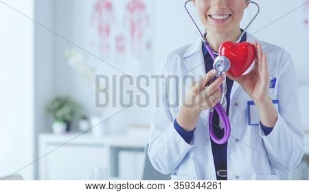 A doctor with stethoscope examining red heart, isolated on white background