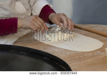 Dough On The Place Table. The Woman Puts Cheese On The Dough. Preparing For Making Pies. Close Up.