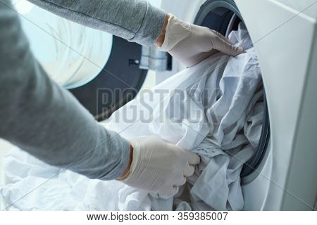closeup of a young caucasian man, wearing latex gloves, putting white bed linen into the washing machine