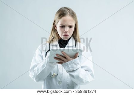 Young Girl In White Lab Coat Squinting At A Clipboard With A Morose Expression As She Pretends To Be