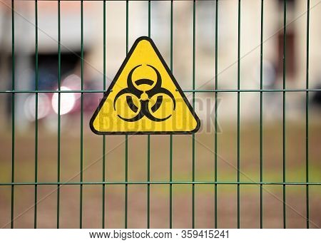 Biohazard Warning Sign On Green Decorative Metal Wire Fence, The City Street Silhouettes Are Visible