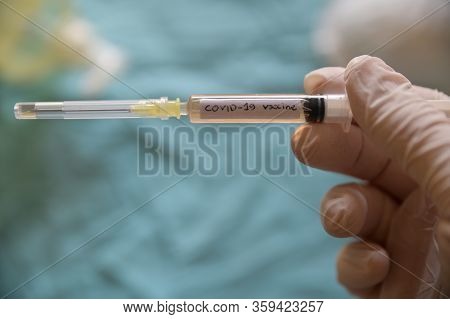 Close Up Shot Of A Syringe With The Word Coronavirus Vaccine.he Is Holding Her Hand With A White Lat