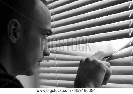 A Young Man Look Out The Window Throgh The Blinds Soft Focus
