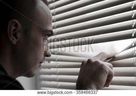 A Young Man Look Out The Window Throgh The Blinds Soft Focus