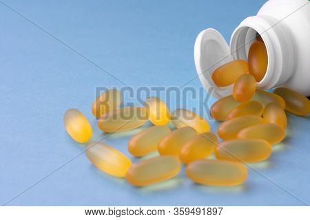 Yellow Chewable Capsules With Fish Oil In Plastic White Jar Are Lying On Blue Background. Omega 3 Pi