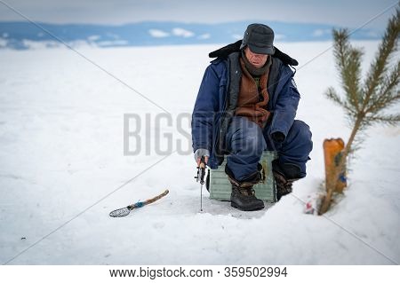 Baikal Lake, Siberia, Russia - March 05, 2020 : Winter Ice Fishing. A Fisherman Is Fishing On Spinin
