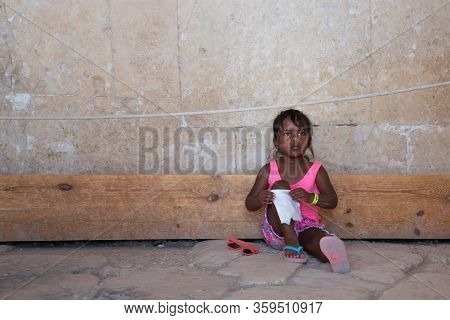 Luxor, Egypt - 29.03.2020: Little Girl Child Sitting Under Wall On The Street