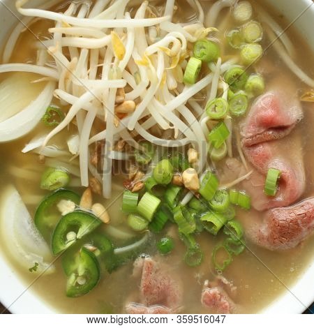 Close up of an asian noodle soup with beef, shives, onion, bean sprout and lime
