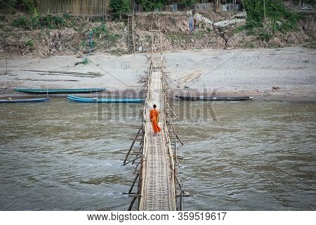 A Alone Monk Crossing A Bamboo Bridge In Luang Prabang