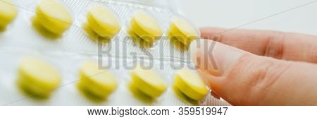 Blister With Yellow Vitamins In Female Fingers Closeup.