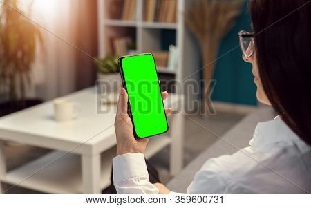Woman Vertically Holding Smartphone With Green Screen Sitting In Flat, Sunlight Through Window
