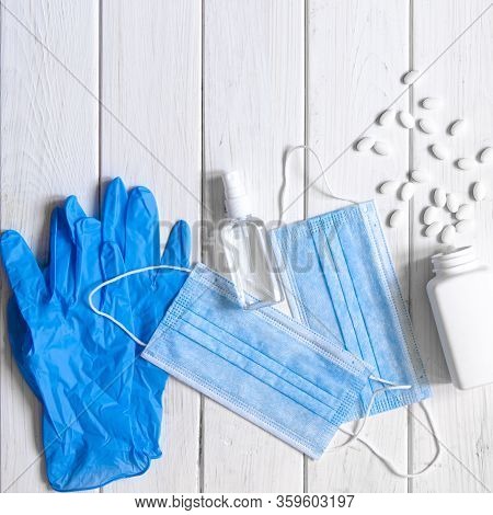 Medical Protective Mask, Rubber Gloves, Antiseptic And White Anti-irus Tablets Lie On A White Wooden