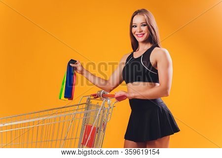 Athletic Girl Performs Exercises Using A Resistance Band. Photo Of Young Girl On Drey Background. St