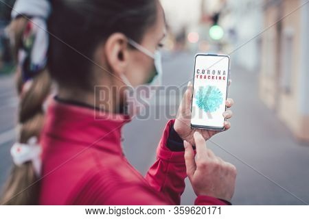 Woman using a phone with the coronavirus tracking app installed walking a city street