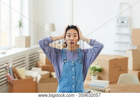 Waist Up Portrait Of Young Asian Woman Panicking While Standing Among Cardboard Boxes In Empty Room 