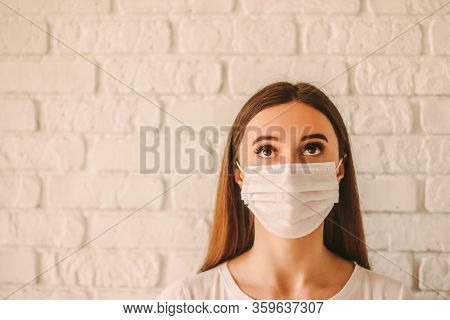 Young Scared Woman In Medical Mask On Face Looking Up At Copy Space. Confident Female Doctor In Prot