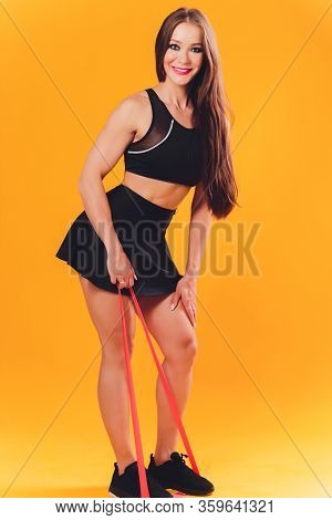 Athletic Girl Performs Exercises Using A Resistance Band. Photo Of Young Girl On Drey Background. St