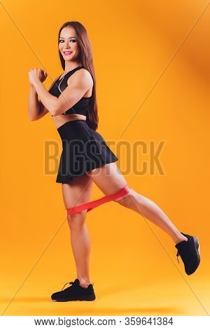 Athletic Girl Performs Exercises Using A Resistance Band. Photo Of Young Girl On Drey Background. St