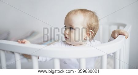 Adorable Baby Girl In Co-sleeper Crib Attached To Parents Bed. Little Kid Sitting In Cot