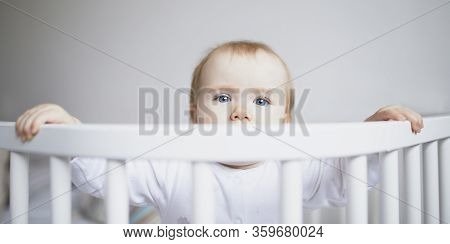 Adorable Baby Girl In Co-sleeper Crib Attached To Parents Bed. Little Kid Sitting In Cot