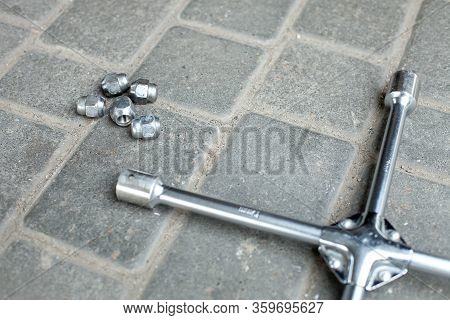 A Wrench For Removing Wheels From A Car With Nuts Lying On The Ground, Closeup Top View.