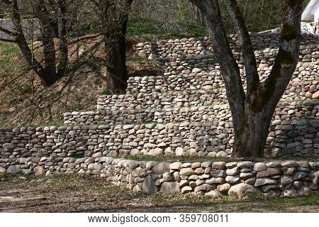 Sunny Spring Day. On A Slope Of The Hill Big Trees Grow And From A Natural Stone Several Retaining W