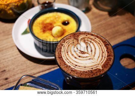 Cafe Latte With Latte Art On A Cup With Vanilla Crème Brûlée On The Background.