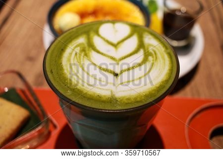 Close Up Image Of Green Matcha Latte With Latte Art On A Glass With Vanilla Crème Brûlée Dessert.