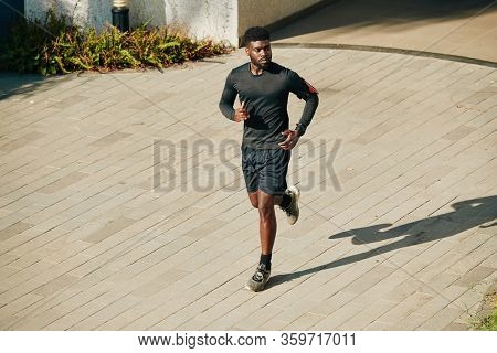 Serious Young African-american Sportsman Running Outdoors In Shorts And Rashguard When Preparing For