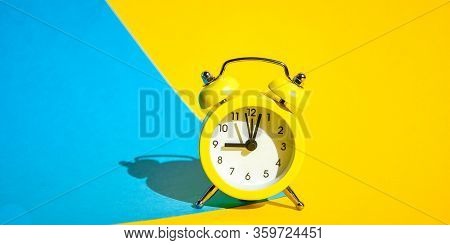 Yellow Vintage Alarm Clock On A Blue And Yellow Background With Selective Focus, Copy Space For Text