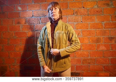 A Middle-aged Woman Poses Showing Clothes Near Red Brick Wall. An Inept Model In An Inept Shoot