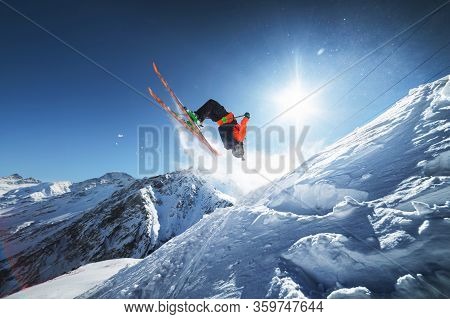 Low Angle View Athlete Skier In An Orange Jacket Does A Back Flip With Flying Powder Of Snow Against