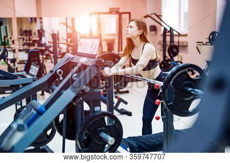 Gorgeous Woman Posing Near Sports Equipment At A Gym Looking Straight In Front Of Her. She Wears Bri