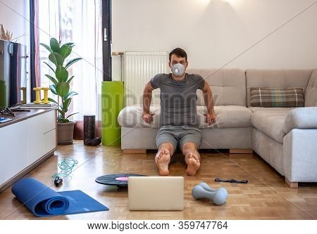 Young Man In Mask On Quarantine Exercising Doing Workout At Home In Front Of Laptop